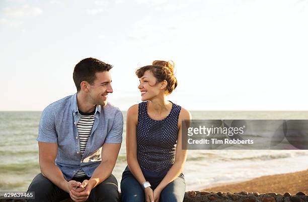 man and woman sat on wall together - faccia a faccia foto e immagini stock