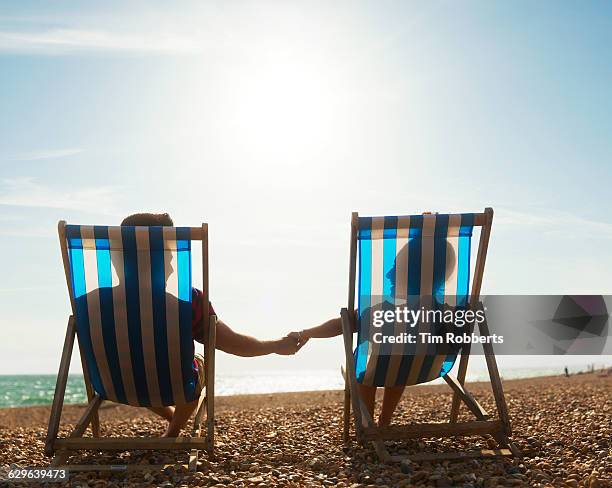 couple holding hands on deckchairs - man on the beach relaxing in deckchair fotografías e imágenes de stock