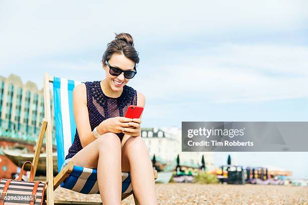 woman using smart phone on deckchair. - camisa sin mangas fotografías e imágenes de stock