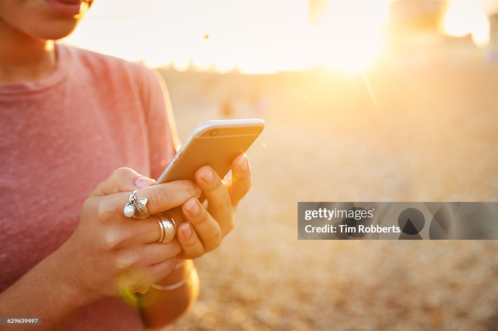 Woman using smartphone at sunset, close up