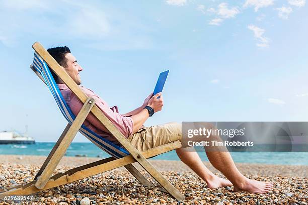 man with tablet at beach. - man on the beach relaxing in deckchair stock-fotos und bilder