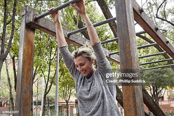 blonde girl swings from monkey bars smiling - monkey bars fotografías e imágenes de stock