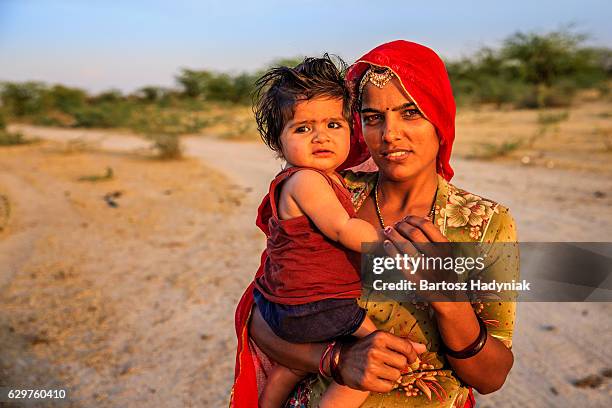 young indian woman holding her little baby, india - village of fatisah stockfoto's en -beelden