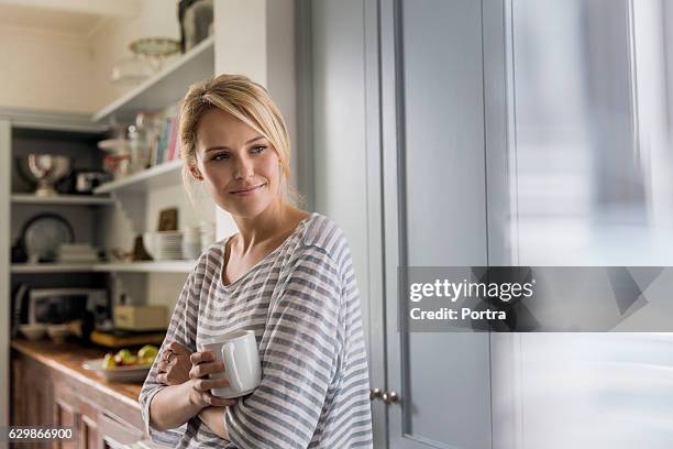 thoughtful woman holding coffee mug by window - blond hair young woman sunshine stock pictures, royalty-free photos & images