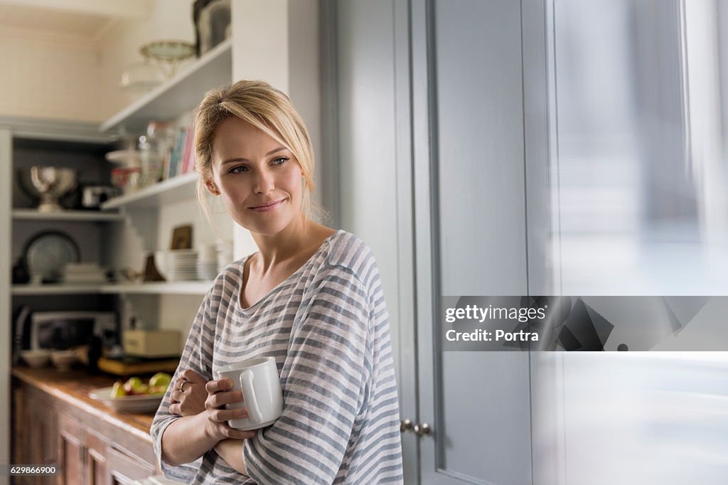 Thoughtful woman holding coffee mug by window