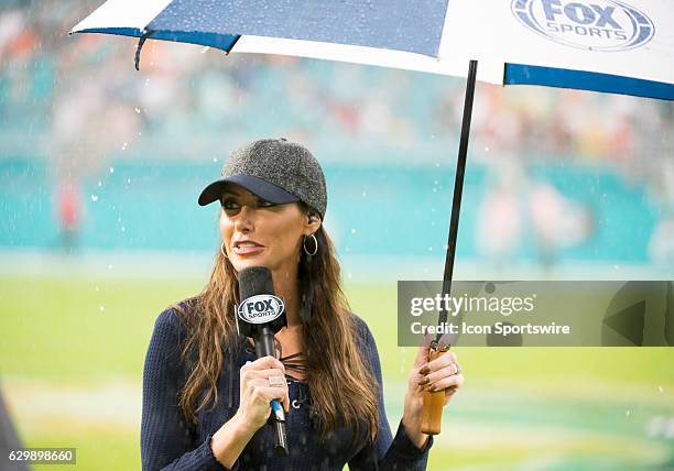 Sports field reporter Holly Sonders holds a microphone and umbrella in the rain on the field after the NFL football game between the Arizona...
