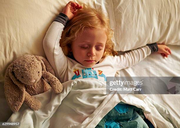 young girl sleepign with stuffed rabbit - kids sleep in bed stock-fotos und bilder