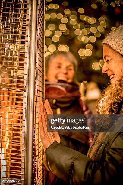 two laughing female friends and fire, night, christmas, carinthia, austria - couple by electric heater stock pictures, royalty-free photos & images