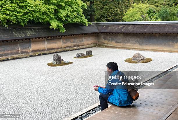 Young man contemplates at Rock zen garden, Ryoanji, Ryoan-ji Temple, Kyoto, Japan.