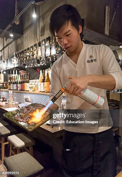 Waiter cooks fresh meat with a blow-torch in a restaurant in Kabukicho, Tokyo, Japan.