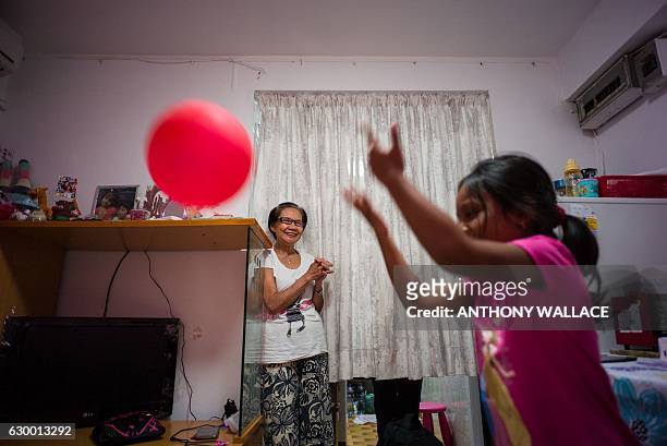 In this photo taken on December 13 four-year-old Keana plays with a balloon, as her elderly grandmother Rosalina smiles in the living of the flat...