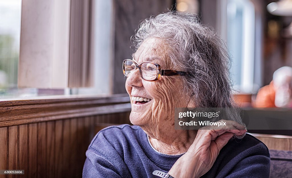 Elderly Smiling Woman With Dementia Looking Out Restaurant Window