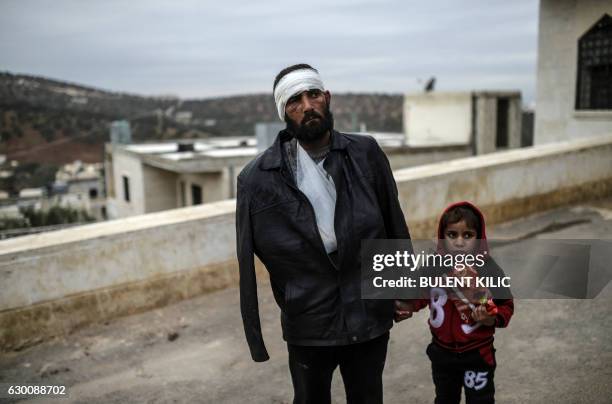 An injured Syrian man who just arrived on the Syrian side of the Bab al-Hawa border crossing between Syria and Turkey waits with his child outside a...