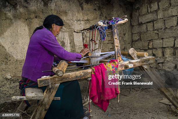 Local woman is weaving material at a loom in open air.