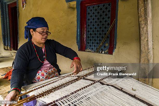 Local woman is weaving a blanket, using sheep wool, in front of a house.