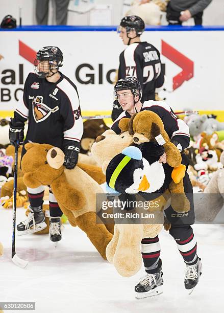 Marcus Kichton and Hunor Torzsok of the Vancouver Giants help pick up teddy bears thrown on the ice during the first period of their WHL game against...