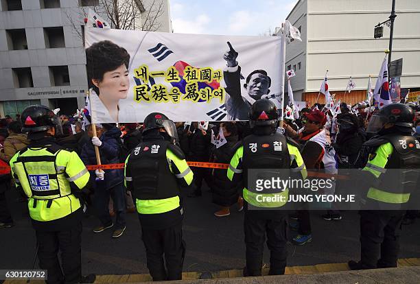 Supporters of South Korea's President Park Geun-Hye carry a large banner showing portraits of President Park and her father, former dictator Park...