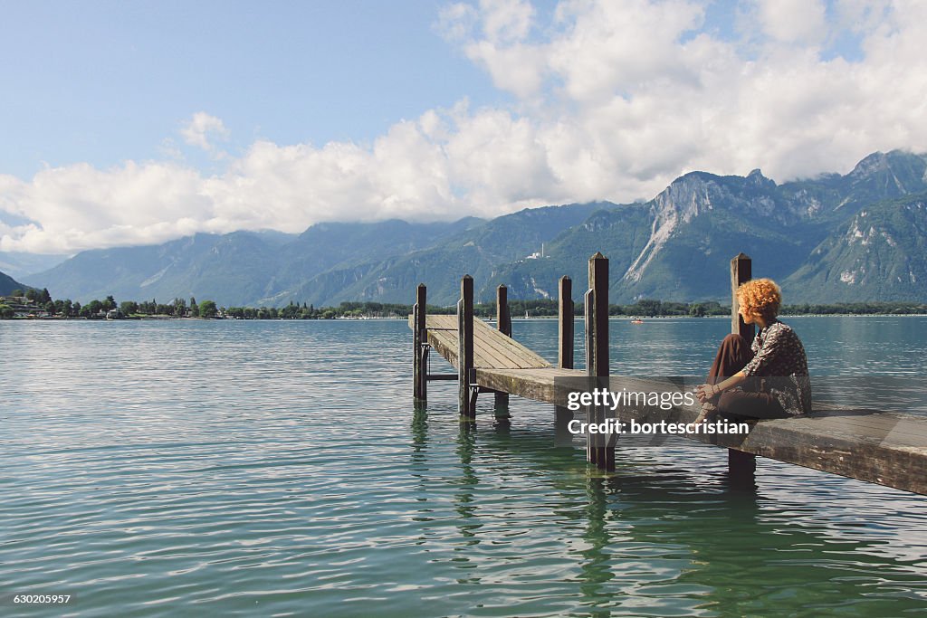 Woman Sitting On Pier Over Lake Against Sky