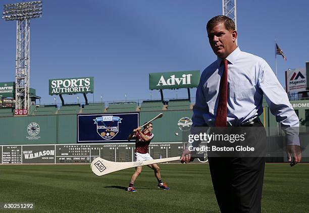 Boston Mayor Martin J. Walsh takes a crack at hurling with Galway team member David Collins, left, after announcing that a hurling match will be held...