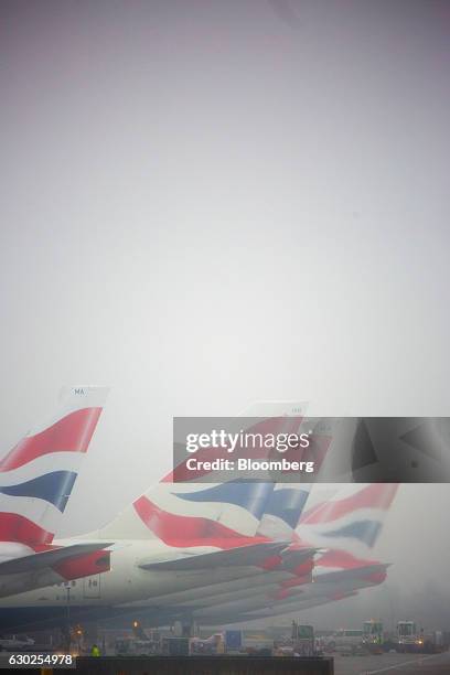 Tail fins on passenger aircraft, operated by British Airways, a unit of International Consolidated Airlines Group SA , stand in fog at Terminal 5 at...