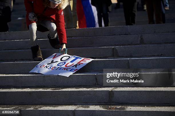 Woman reaching for her dropped sign, joining Donald Trump protestors demonstrating outside the Pennsylvania Capitol Building before electors arrive...