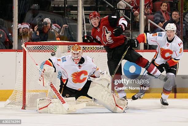 Goalie Brian Elliott of the Calgary Flames makes a save on a shot as Lawson Crouse of the Arizona Coyotes and Jyrki Jokipakka of the Flames battle in...