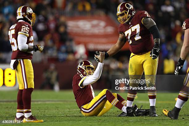 Guard Shawn Lauvao of the Washington Redskins helps teammate quarterback Kirk Cousins up off of the field in the third quarter against the Carolina...