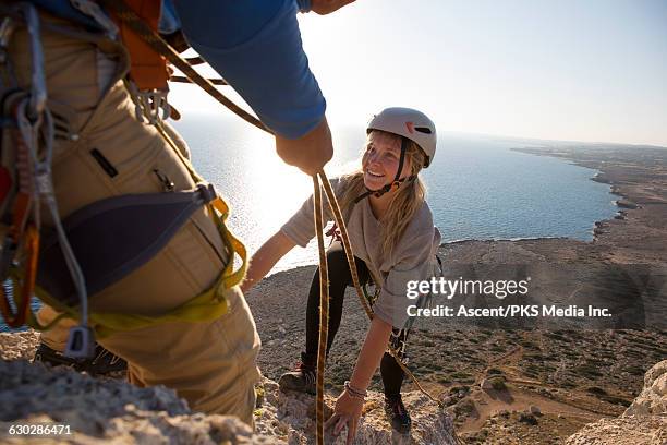 leader belays young woman up rock ridge, sea below - cyprus stock pictures, royalty-free photos & images