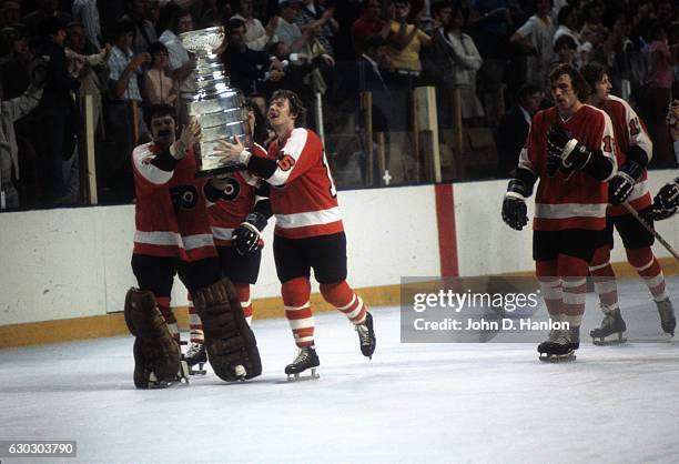 Philadelphia Flyers Bobby Clarke victorious, skating with goalie Bernie Parent holding Stanley Cup trophy after winning game and series vs Buffalo...