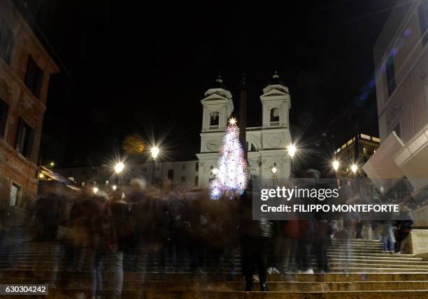 People walk past an illuminated Christmas tree displayed on Piazza di Spagna near the church of the Trinita dei Monti, in central Rome on December...