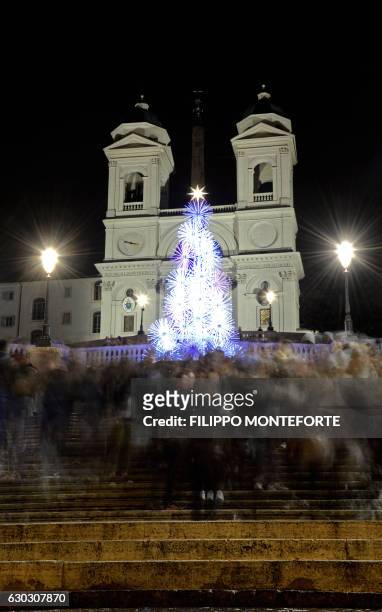 People walk past an illuminated Christmas tree displayed on Piazza di Spagna near the church of the Trinita dei Monti, in central Rome on December...