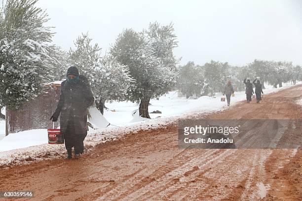 Syrians walk on a muddy road after receiving food aid in plastic buckets at a tent city as it snows in the Azaz town of Aleppo, Syria on December 21,...
