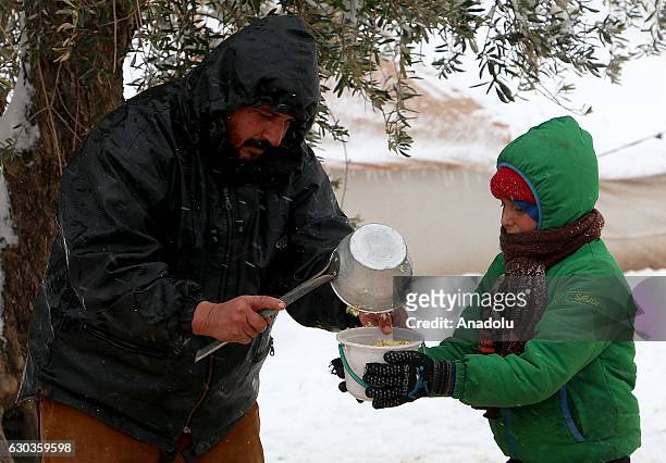 Syrian boy receives food aid in a plastic bucket at a tent city as it snows in the Azaz town of Aleppo, Syria on December 21, 2016.