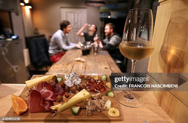 Glass of champagne is served with cheese and ham as guests sit together at a table at the bar 'Aux 3 p'tits bouchons' in Reims, northeastern France,...