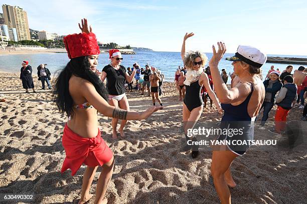 Tahitian performer dances with people taking part in the traditional Christmas Swim in Monaco on December 24, 2016. / AFP / Yann COATSALIOU