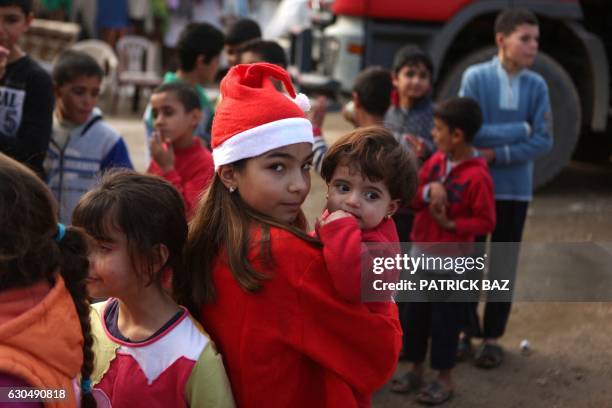 Chloe, a Lebanese Christian teenager dressed as Santa Claus, holds a Syrian refugee on December 24, 2016 during a gift distribution organised by the...