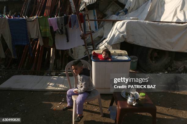 Syrian refugee child sits on a chair as another stands inside a washing machine placed outside their makeshift home in a slum on December 24, 2016 in...