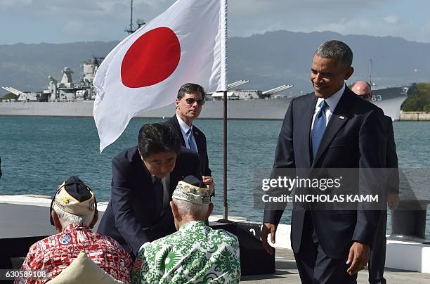 President Barack Obama looks on as Japanese Prime Minister Shinzo Abe shakes hands with veterans at Kilo Pier overlooking the USS Arizona Memorial on...