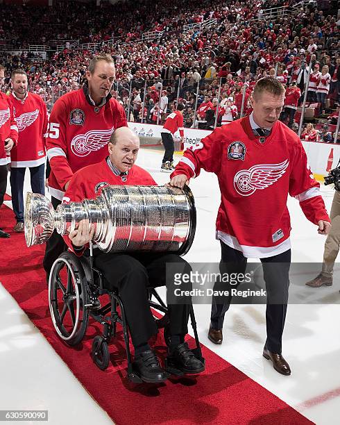 Vladimir Konstantinov holds the Stanley Cup as former teammates Darren McCarty and Kris Draper help him off the ice after the ceremony for the...