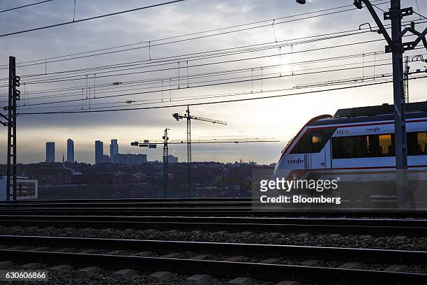 Passenger train, operated by Renfe Operadora SC, travels along rails past the skyscrapers of the Cuatro Torres business district in Madrid, Spain, on...