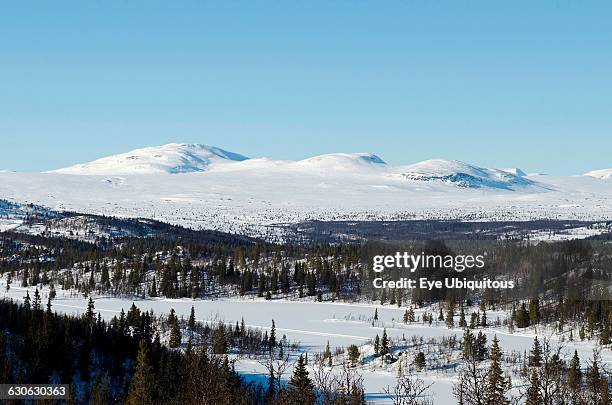 Norway, Central Region, Buskerud County, View of Vindhaugen peak with frozen lake and forested areas in foreground.