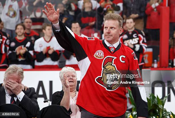 Daniel Alfredsson salutes the crowd during his jersey retirement ceremony as his parents look on in the background prior to a game between the Ottawa...