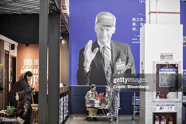 Customers arrange a shopping cart in front of an advertisement featuring the photograph of Wal-Mart Stores Inc. Founder Sam Walton at the company's...