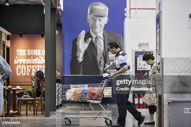 Customer pushes a shopping cart in front of an advertisement featuring the photograph of Wal-Mart Stores Inc. Founder Sam Walton at the company's...