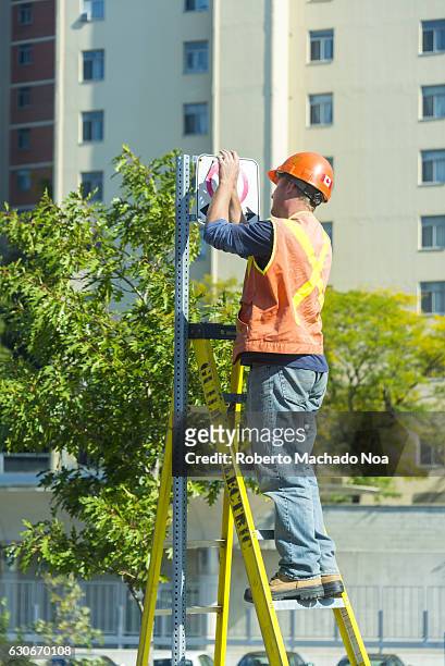 Utility man working on a traffic sign. There are trees and buildings behind the sign.