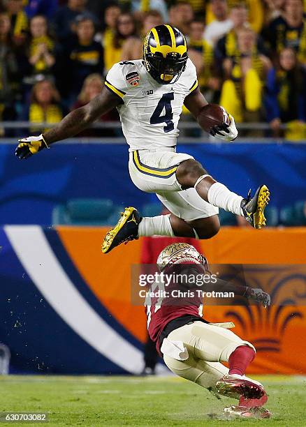 De'Veon Smith of the Michigan Wolverines leaps over Marquez White of the Florida State Seminoles in the third quarter during the Capitol One Orange...