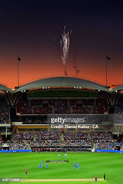 The Strikers players celebrate the fall of a wicket as fireworks can be seen at sunset during the Big Bash League match between the Adelaide Strikers...