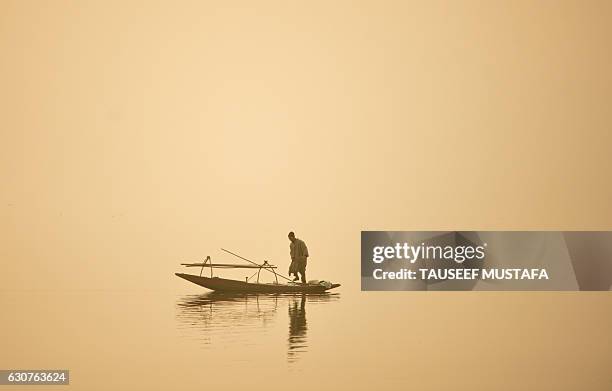 Fisherman walks on his boat during a dense fog day on the Dal Lake in Srinagar on January 1, 2017. / AFP / TAUSEEF MUSTAFA