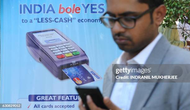 An Indian bank teller checks his phone as he walks past a poster advertising electronic payments at a Digital Wealth Fair in Mumbai on January 3,...