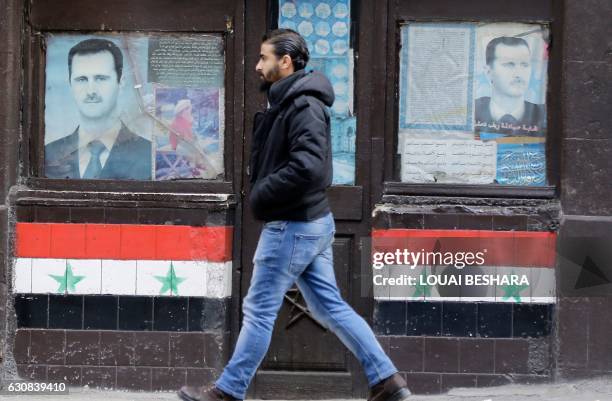 Syrian man walks past posters of Syrian President Bashar al-Assad on a shop front in the capital Damascus on January 3, 2017.